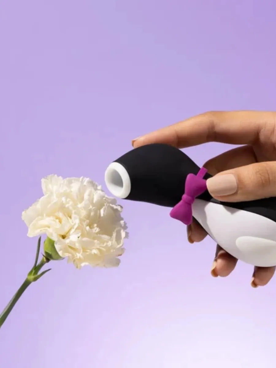 Black air pulse massager held beside a white carnation on a lilac background
